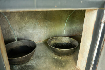 Fototapeta premium Old dark metal cauldron resting inside empty rustic concrete fireplace niche creating eerie quiet abandoned gloomy feeling in historical kitchen architecture