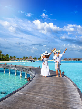 Rear view of a happy family standing on a pier over turquoise ocean and enjoying their tropical holidays in the tropical Maldives islands