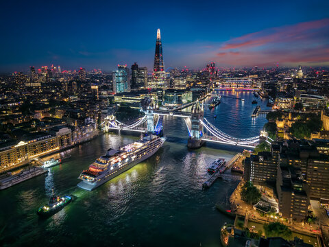 Aerial view of the skyline of London with a motion pasenger ship passing under the lifted Tower Bridge during twilight, England