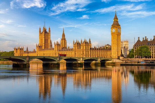 Beautiful summer sunrise view of the Westminster Palace and Big Ben clocktower in London, England, with reflections in the River Thames