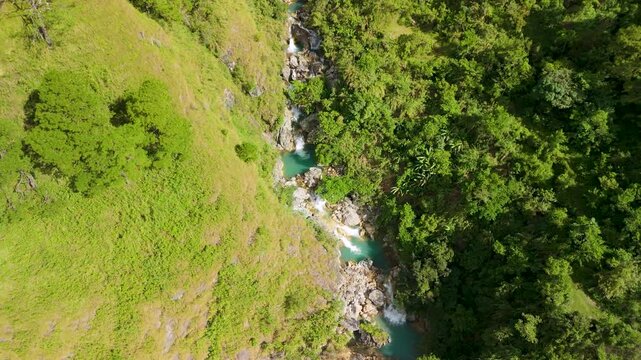Aerial tilt-up from Sagada Blue Lagoon turquoise cascades reveals lush mountain landscape with scattered hillside houses and rolling peaks in Philippines