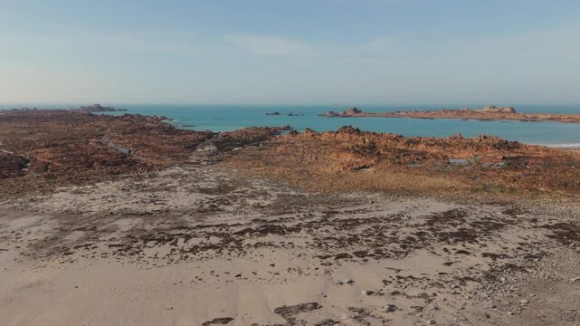 Cobo Bay Guernsey Channel Islands.Panning drone footage of sandy beach and rocky foreshore on northern shore of bay with views out to sea across rocky outcrops in late afternoon sun