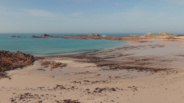 Cobo Bay Guernsey Channel Islands.Panning drone footage of sandy beach and rocky foreshore with golden sand and seaweed on the shoreline and views out to in golden late afternoon sun