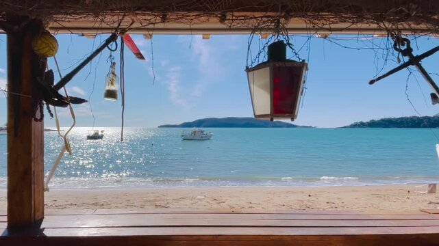 Rustic beach shack window frames turquoise sea, hanging lantern and ropes, fishing nets drying, small boats anchored near island,