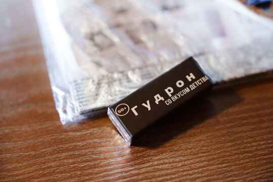 2026.04.30, Russia. Macro view of a nostalgic black tar chewing gum bar next to its original vintage style packaging paper wrapper on a wooden table.
