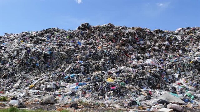 View shows a large garbage dump with various piles of plastic and household trash under a clear blue sky during the day