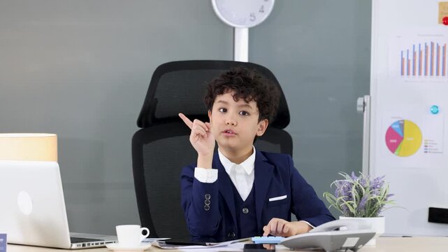 Young Boy in Business Suit Using Calculator and Pointing in Office