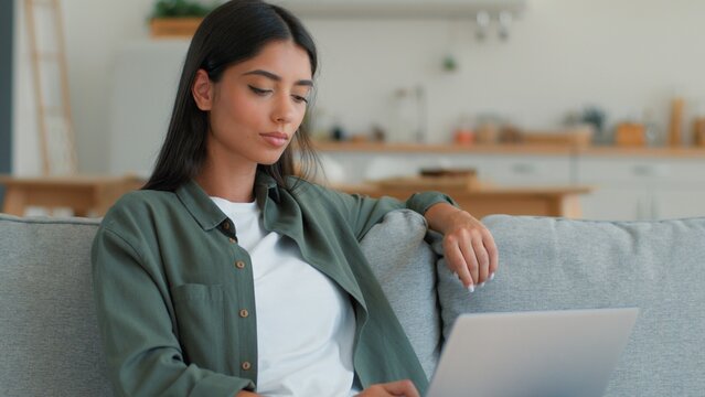 Pensive Indian woman using laptop computer thinking typing freelancer at home student Arabian female ethnic girl businesswoman browsing online shopping booking food delivery order internet app indoors