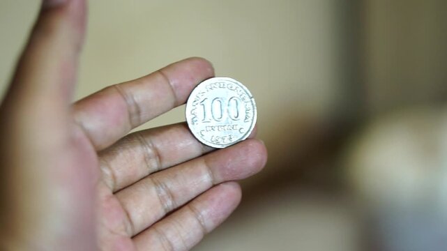 Hand holding a vintage 100 rupiah coin with detailed classic Indonesian currency design.	