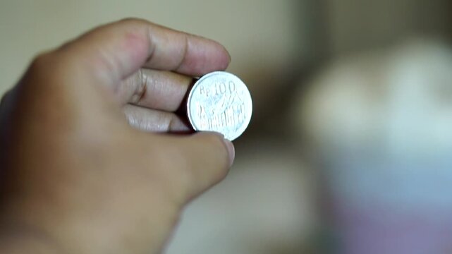 Hand holding a vintage 100 rupiah coin with detailed classic Indonesian currency design.	