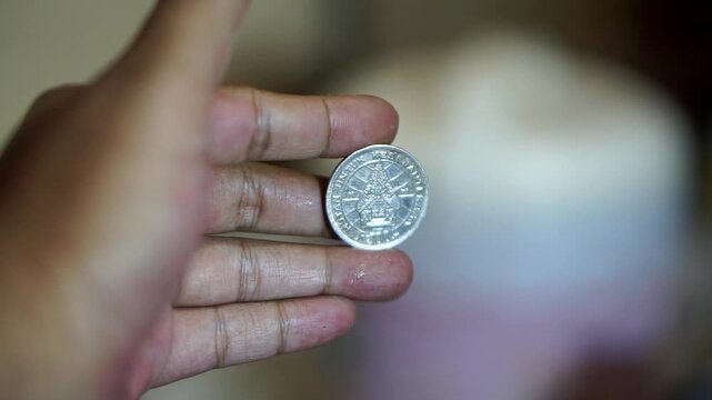 Hand holding a vintage 100 rupiah coin with detailed classic Indonesian currency design.	