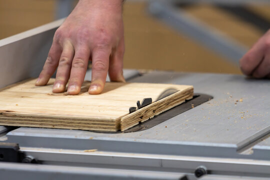 Canada, 14 April 2026 : Carpenter's hand guides plywood through a table saw in a workshop