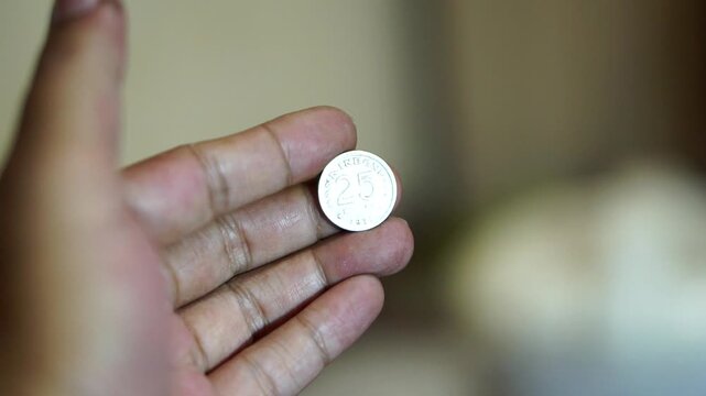 Hand holding a vintage 25 rupiah coin with detailed classic Indonesian currency design.	