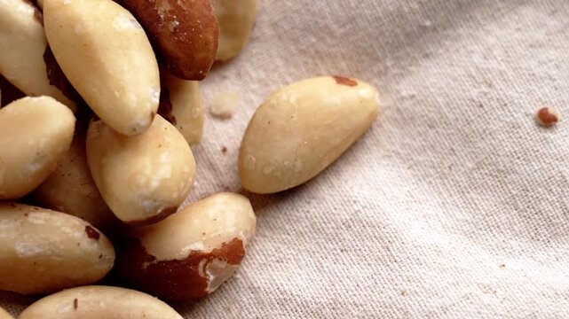 Fingers selecting a Brazil nut from a pile of mixed kernels on textured fabric surface. Concept of healthy snacks
