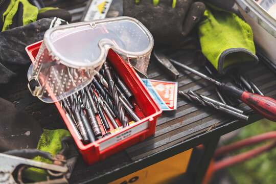 Assorted workshop tools including welding helmet and cutting discs placed on a wooden stool outdoors. Industrial DIY and metalworking equipment in natural light.