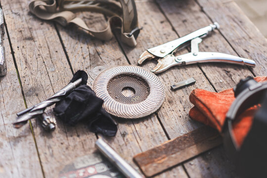 Assorted workshop tools including welding helmet and cutting discs placed on a wooden stool outdoors. Industrial DIY and metalworking equipment in natural light.