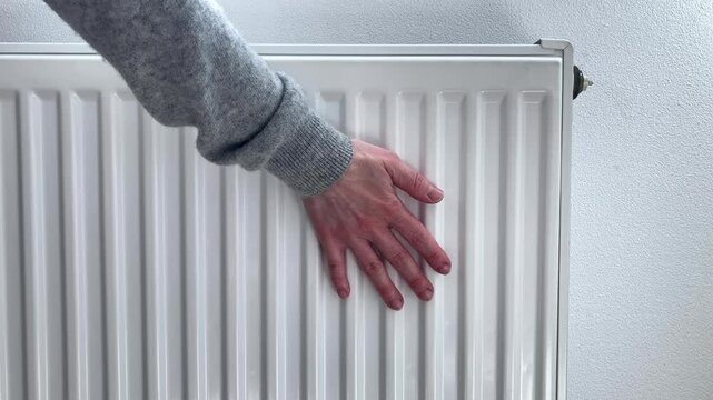 Woman checks temperature of radiator. A woman's hand in gray knitted sweater touches te heater. Taking care of comfort in the house and monitoring the operation of heating system in cold season
