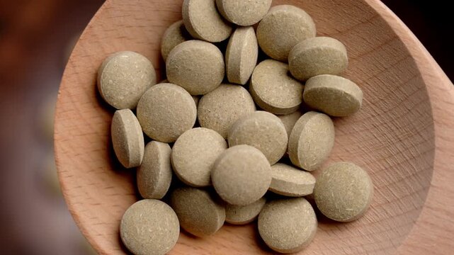 Closeup of natural cat grass supplement tablets arranged in a wooden spoon with detailed herbal texture