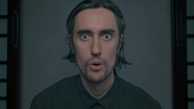 Yakuza handsome guy surprised shocked stunned, calm indoor portrait of man with gray hair and beard in dark shirt, minimalist setting, subtle expressions facing camera