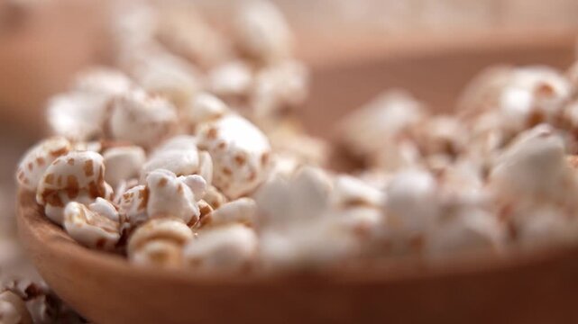 Macro of a man fingers taking a pinch of puffed buckwheat grains from a wooden spoon. Concept of healthy breakfast preparation