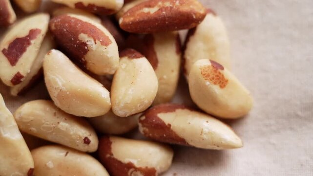 Peeled organic Brazil nuts heap on beige fabric background close up. High quality source of selenium, healthy fats and nutrients. Rotation
