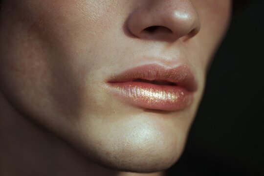 Close crop of male lips with gold shimmer makeup for beauty editorial and skincare detail on mouth and philtrum