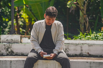 Obraz premium Thoughtful man sitting reading a note on steps outdoors in a park in daytime