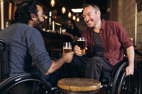 Two friends in wheelchairs enjoying beer together at bar