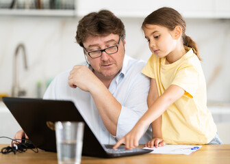 Fototapeta premium Little daughter shows her father how to use laptop