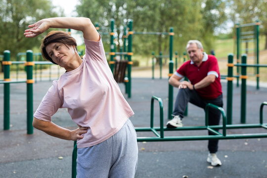 elderly woman does gymnastics on an outdoor sports ground