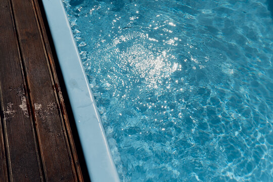 The clear blue water in the outdoor pool glistening in the sunlight and the wooden deck around the pool 