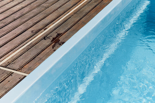 The clear blue water in the outdoor pool glistening in the sunlight and the wooden deck around the pool 