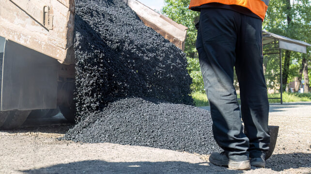 Dump truck unloading fresh hot asphalt on a street during road construction work with a worker standing nearby