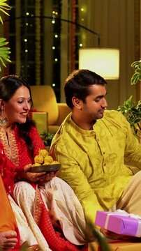 Clicking Diwali selfie with laddu, Indian family with young girl, senior mother in saree, old father and husband in traditional wear celebrating Hindu festival at decorated home with diya rangoli