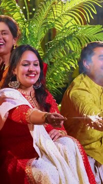 Enjoying sparkles on Diwali night, Indian family with young girl, senior mother in saree, father and husband in traditional dress sitting on festive steps with diya, flower rangoli, firecrackers joy