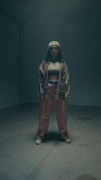 Vertical shot of young female dancer entering shot and starting dynamic hip hop choreography facing camera in studio lit by flashing lights, social media story format