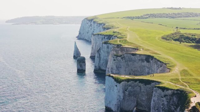 Aerial drone footage flying over Old Harry Rocks and the white chalk cliffs on the Dorset coastline in England. The shot shows dramatic sea stacks, green clifftop paths, blue sea, and the surrounding