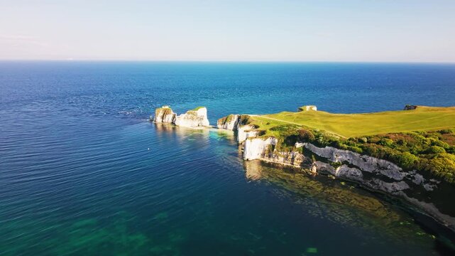 Aerial drone footage of Old Harry Rocks on the Dorset coast in England, showing white chalk sea stacks, dramatic coastal cliffs, green clifftop grass, and clear blue sea.