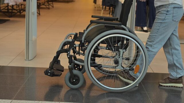 A faceless woman pushes a wheelchair through a shopping mall.