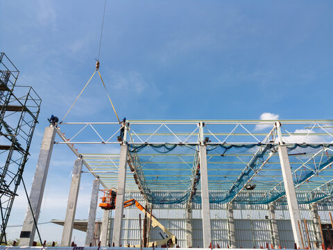 Mobile crane lifts steel roof truss frame into position during factory warehouse construction project, symbolize progress, productivity and advanced building techniques in industrial construction.