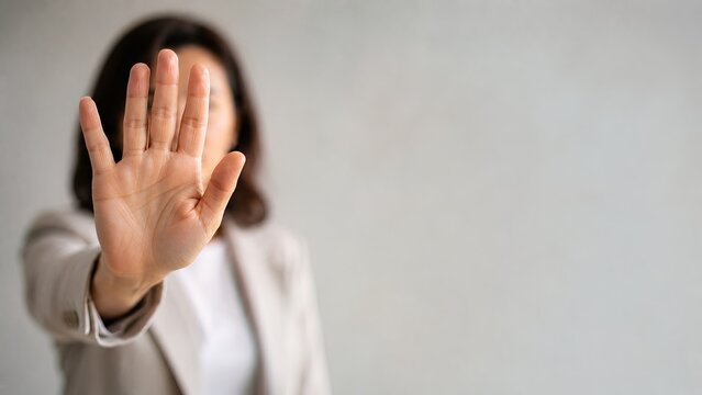 Businesswoman extending hand in a stop gesture against a gray background.