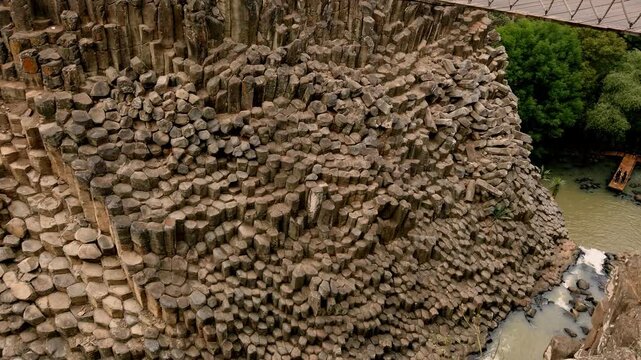 Close view of massive basalt rock formations and geometric volcanic columns inside natural canyon landscape in Mexico during daytime.