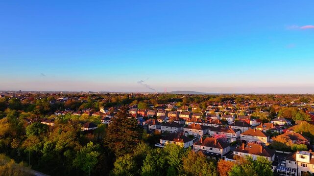 Sunlit Dublin suburb with rows of houses and a distant smokestack under a clear sky. Suitable for urban landscape projects or real estate promotions.