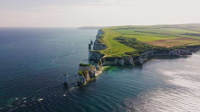 Wide aerial drone footage of Old Harry Rocks on the Jurassic Coast in Dorset, England, showing white chalk cliffs, sea stacks, green clifftop paths, surrounding farmland, and calm blue sea.