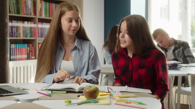 Angry Caucasian teen girls arguing conflict at desk indoors classroom quarrel discussion schoolgirls students classmates teenagers disagreement studying homework exam education stress school argument