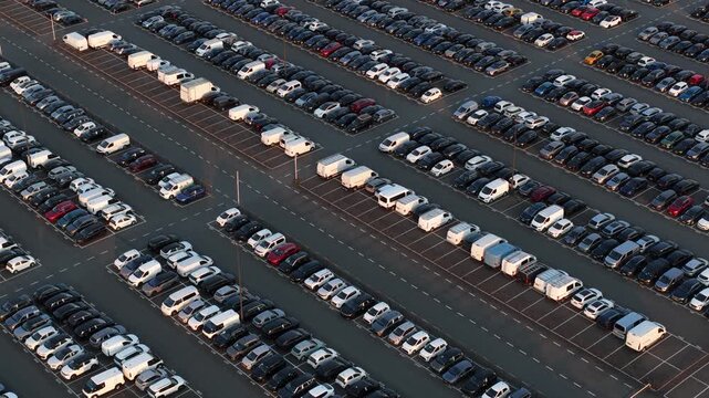 High angle view showing hundreds of brand new cars and vans perfectly aligned in a massive parking lot at a vehicle manufacturing plant, waiting for shipping and distribution to dealers