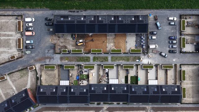 High angle top down aerial showing modern townhouses under construction, featuring rooftops with solar panels and green roofs amidst ongoing landscaping and groundwork in a new housing estate