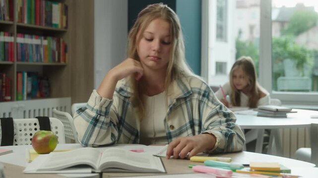 Bored sad Caucasian teen school girl studying in classroom reading book tired student desk exhausted frustrated pupil learning lesson education schoolgirl child boring study hard task teenager indoor