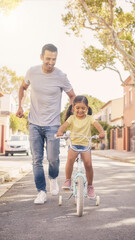 Fototapeta premium Father teaching his daughter to ride a bicycle on a suburban street, happy man running alongside a little girl pedaling a bike with training wheels, vertical shot
