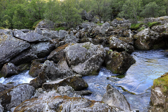 Landscape photo with a view of a fast mountain river and large rocks along the trekking path to Lake Bondhusvatnet in Norway